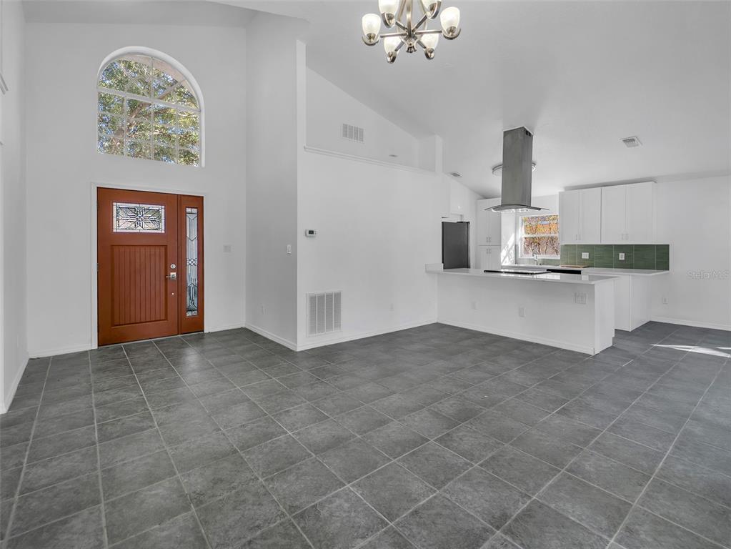 An open-concept room features gray tile flooring, a wooden front door, and a modern kitchen — 11606 GOODWYCK DRIVE, ORLANDO, FL