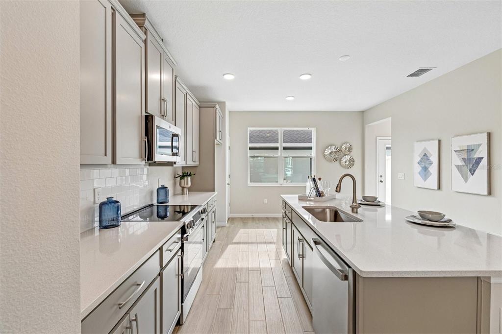 A modern kitchen features light gray cabinets, white quartz countertops, and wood-look tile flooring — 1402 MOUNT ROYAL DRIVE, ST CLOUD, FL