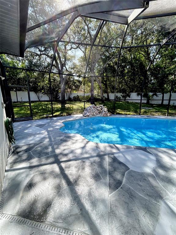 A swimming pool with a stone deck is enclosed by a screened lanai in a backyard — 18608 AUTUMN LAKE BOULEVARD, HUDSON, FL