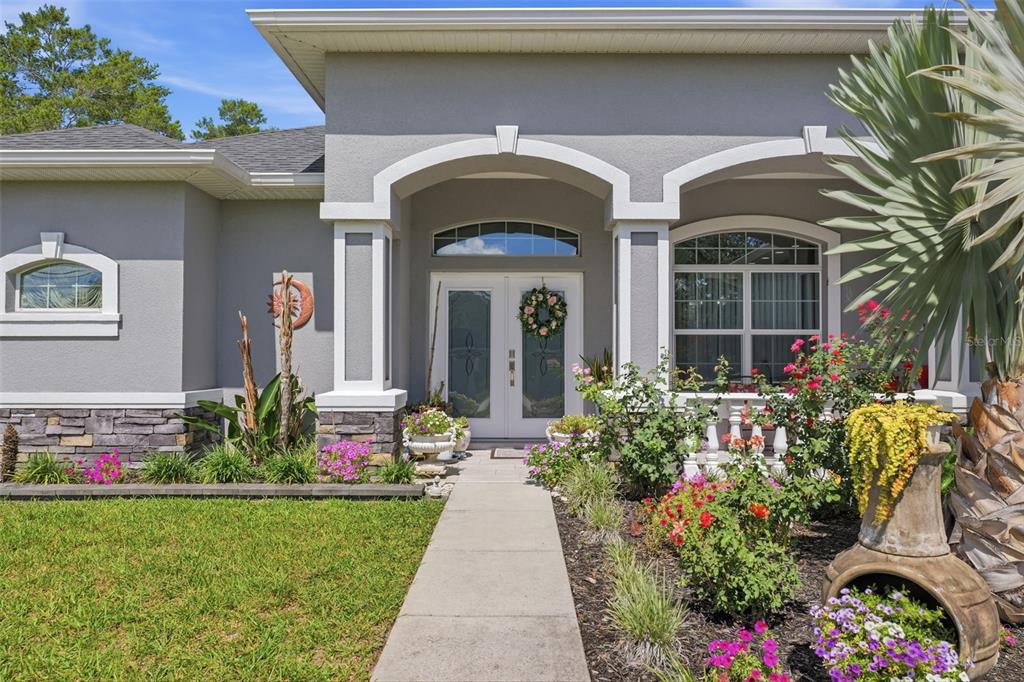 A gray house exterior features a stone-accented base, white columns, and a landscaped front walkway — 13079 HARRIS HAWK ROAD, BROOKSVILLE, FL