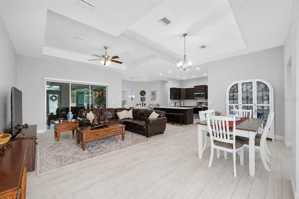 An open-concept living and dining area features light wood floors, a tray ceiling, and kitchen — 13079 HARRIS HAWK ROAD, BROOKSVILLE, FL