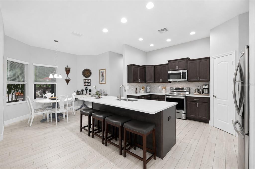 A modern kitchen features dark wood cabinets, a white quartz island, and light wood-look flooring — 13079 HARRIS HAWK ROAD, BROOKSVILLE, FL
