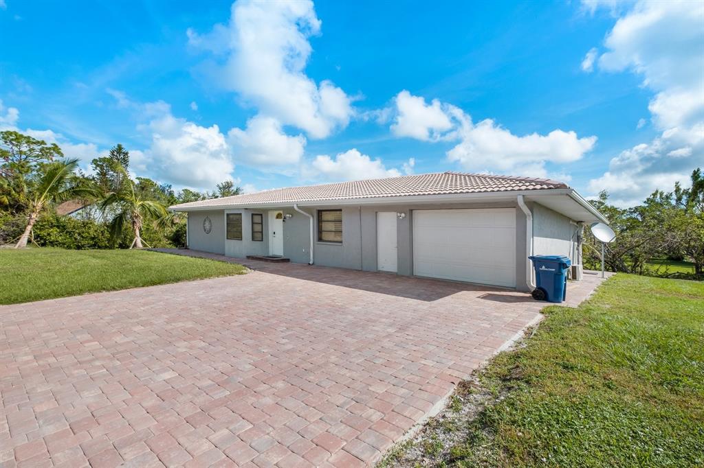 A single-story house with a paved driveway, a two-car garage, and a light-colored exterior — 9080 CALOOSA DRIVE, VENICE, FL