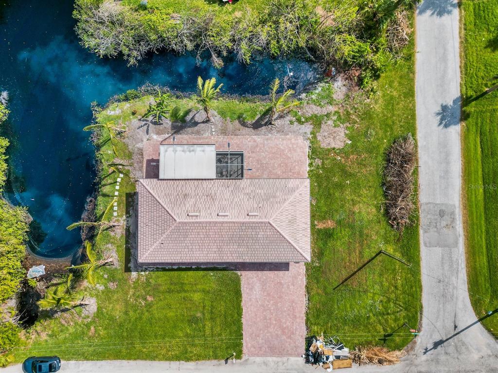 An aerial view shows a house with a tiled roof, patio, and pool beside a canal — 9080 CALOOSA DRIVE, VENICE, FL