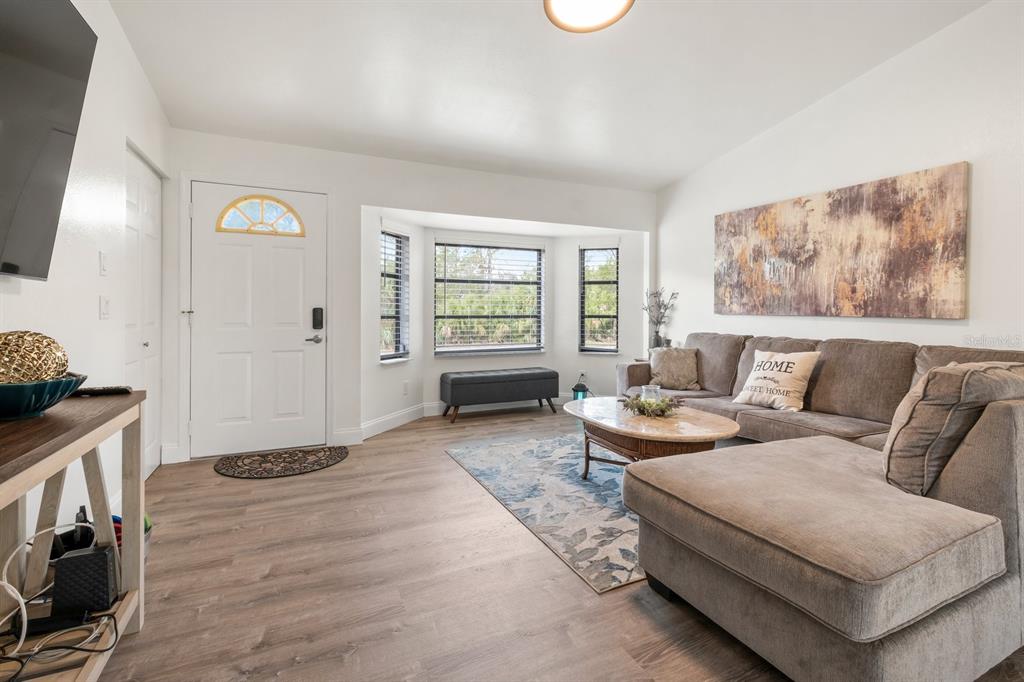A living room features light wood-look flooring, a gray sectional sofa, and a bay window — 9080 CALOOSA DRIVE, VENICE, FL