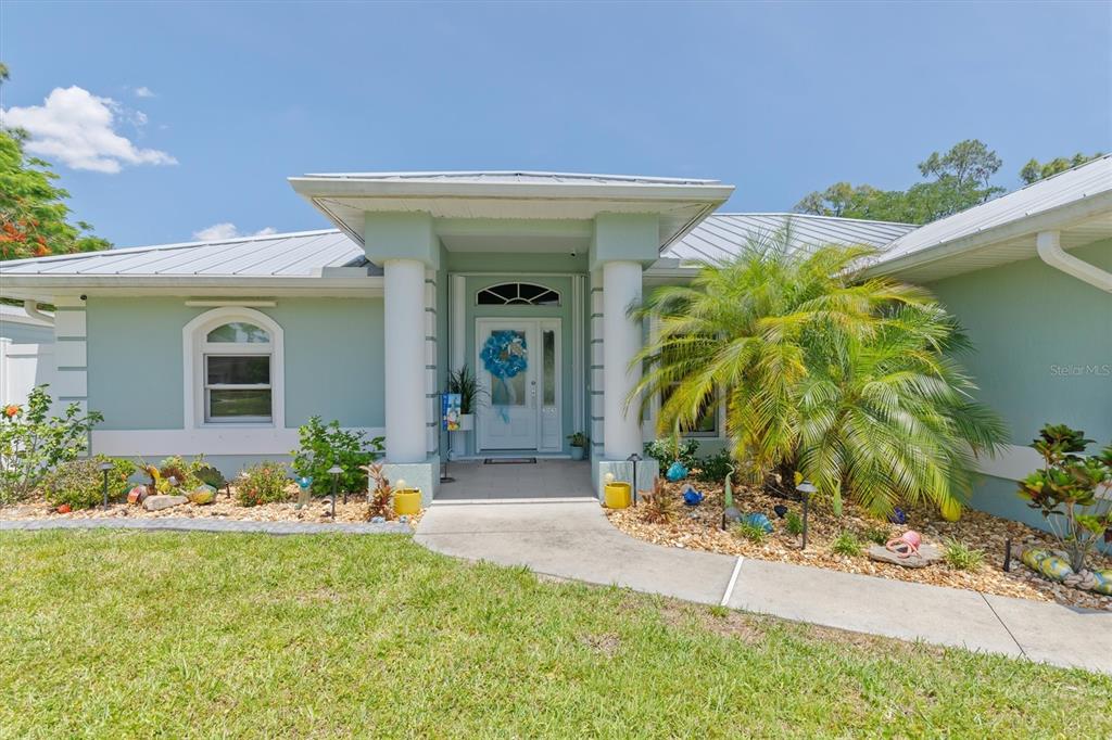 A light green house with a metal roof and a columned entryway under a blue sky — 1636 GLENAN ROAD, NORTH PORT, FL