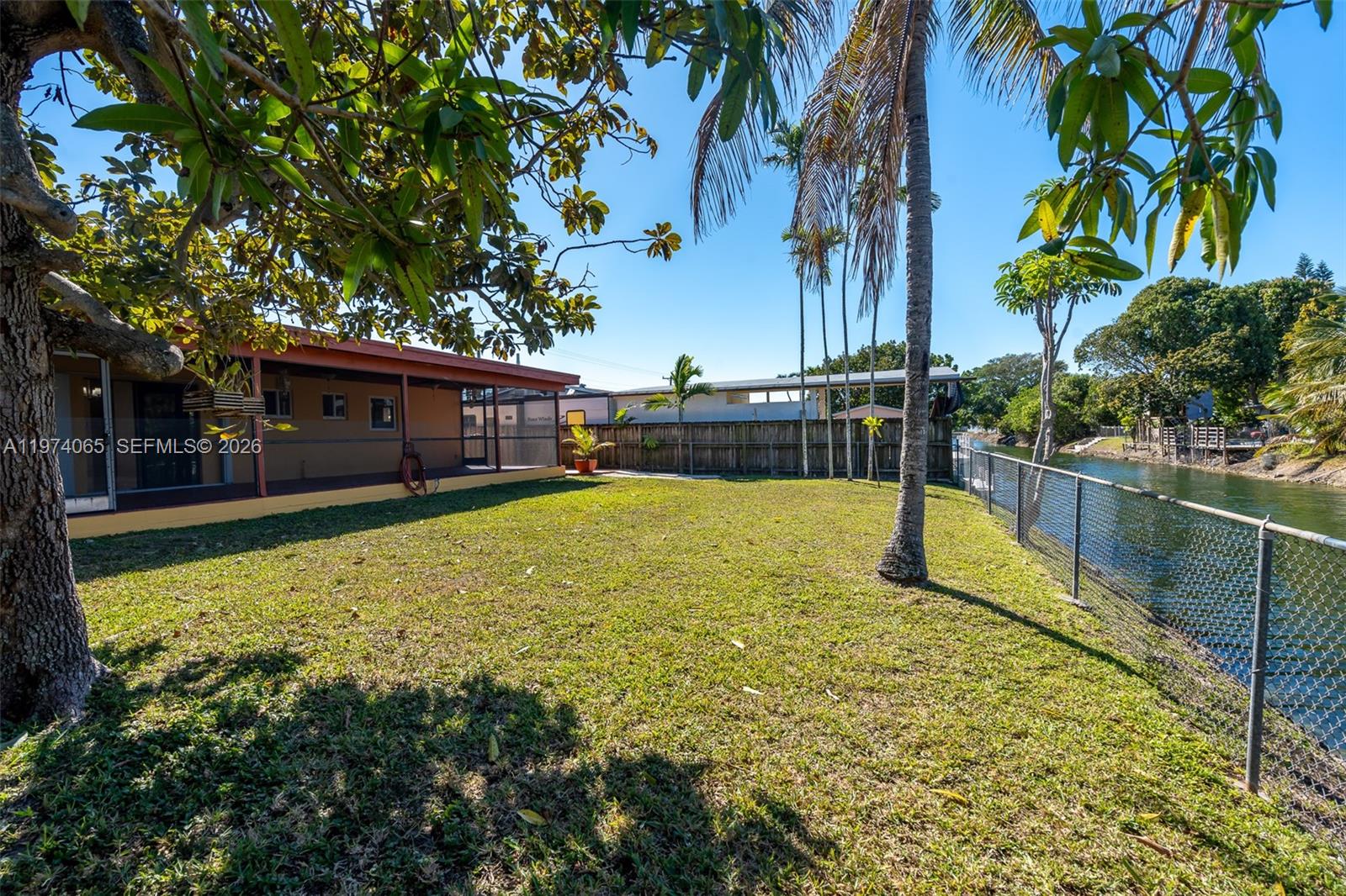 A grassy backyard features a screened-in patio, palm trees, and a chain-link fence along a canal — 4600 SW 104th Ave, Miami FL 33165, MIAMI, FL