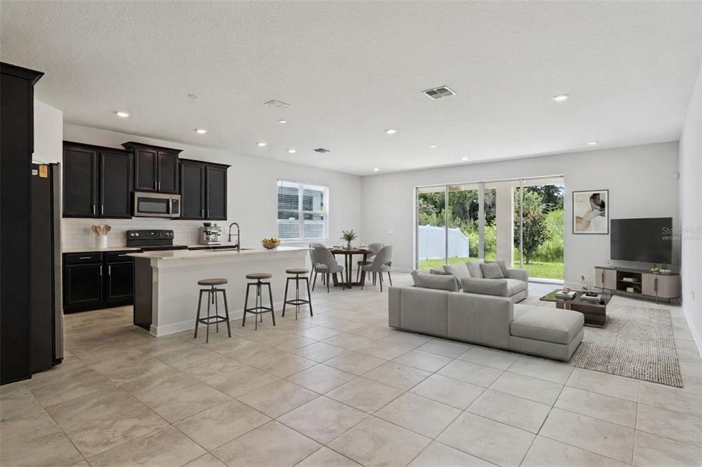 An open-concept kitchen and living area featuring dark cabinetry, a breakfast bar, and tile flooring — 2369 CRESCENT MOON STREET, KISSIMMEE, FL