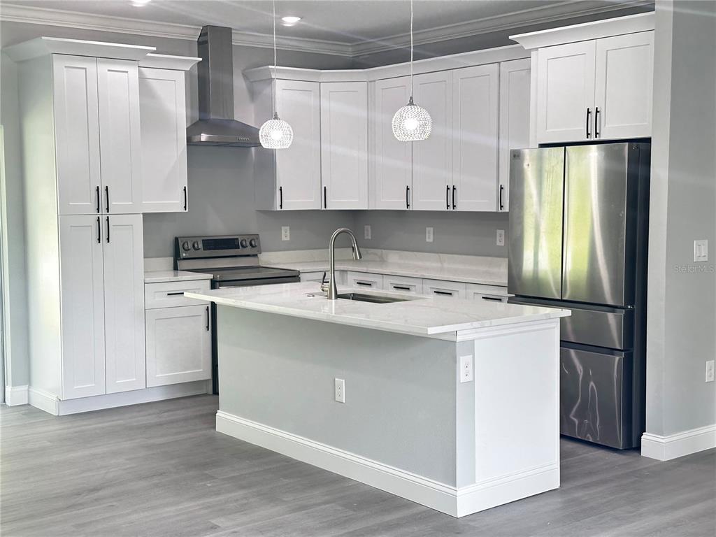 A modern kitchen features white cabinetry, stainless steel appliances, and a central marble-topped island — 221 W EUCLID AVENUE, DELAND, FL