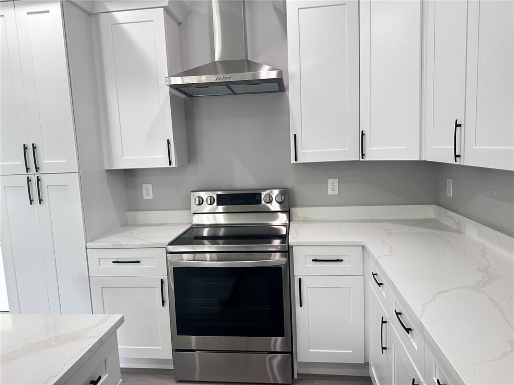 A kitchen features white cabinets, stainless steel appliances, and white countertops with grey veining — 221 W EUCLID AVENUE, DELAND, FL