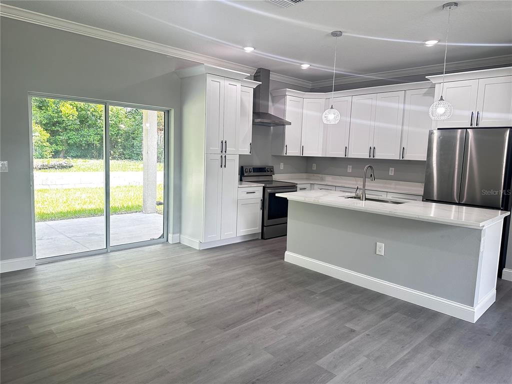 A modern kitchen features white cabinets, stainless steel appliances, a center island, and gray flooring — 221 W EUCLID AVENUE, DELAND, FL