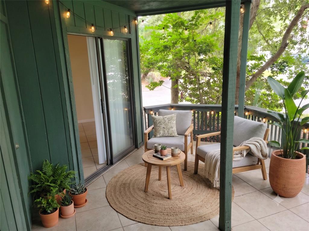 A covered balcony features two armchairs, a round wooden table, and potted plants on tile — 4322 LAKEWAY DRIVE UNIT 13F, ORLANDO, FL