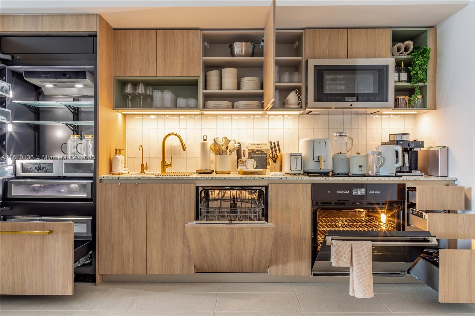 A modern kitchen features light wood cabinetry, gold fixtures, stainless steel appliances, and under-cabinet lighting — 159 NE 6th St # 3615, Miami FL 33132, MIAMI, FL