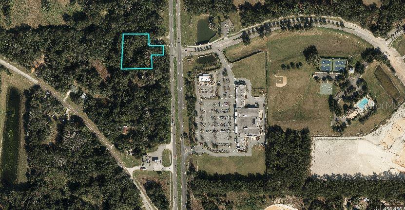 An aerial view shows a wooded lot outlined in blue next to a commercial area — 6714 N ORANGE BLOSSOM TRAIL, MOUNT DORA, FL