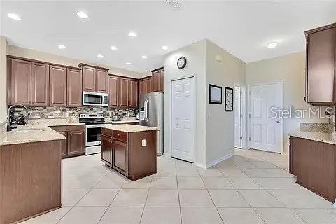 A kitchen features brown wooden cabinets, granite countertops, a center island, and stainless steel appliances — 589 BLUE CYPRESS DRIVE, GROVELAND, FL