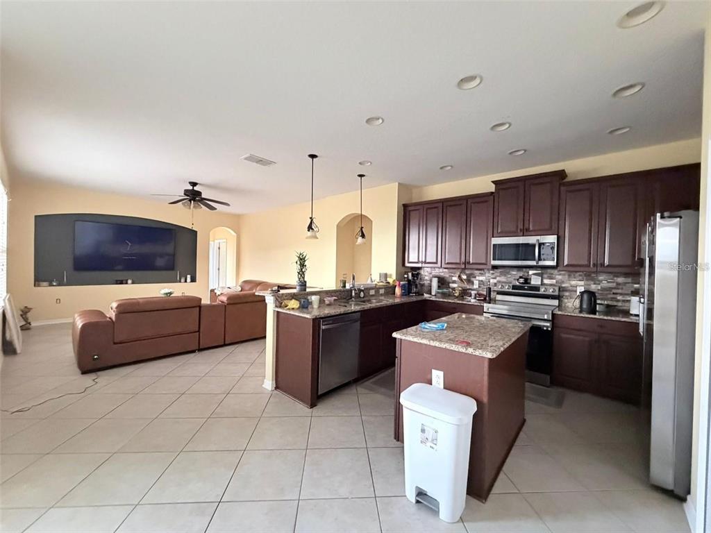 An open-concept kitchen with dark wood cabinets and granite countertops overlooks a living area — 589 BLUE CYPRESS DRIVE, GROVELAND, FL
