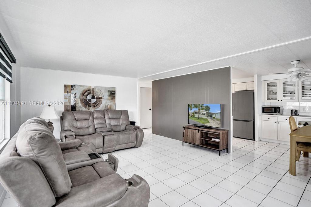 A living room with gray reclining sofas, white tile floors, and an open kitchen — 3495 Tee Terrace, Pompano Beach FL 33069, POMPANO BEACH, FL