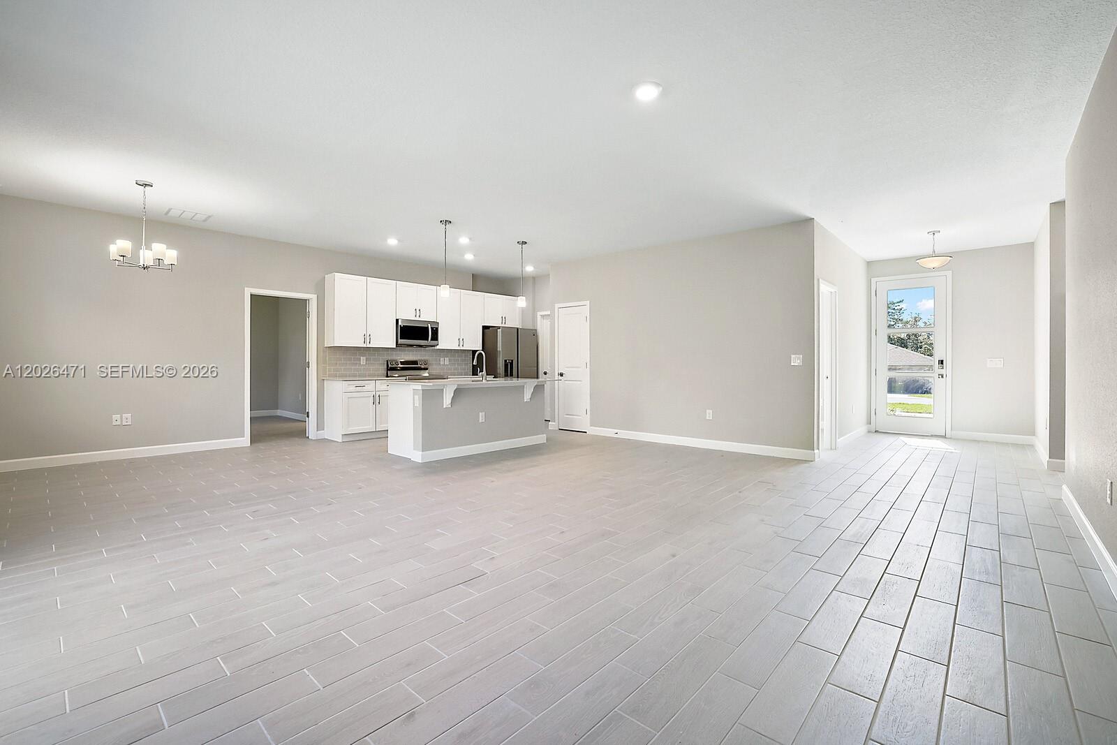 An open-concept kitchen with white cabinets and a center island overlooks a large living area — 950 BARTRAM AVE SW, Palm Bay FL 32908, PALM BAY, FL