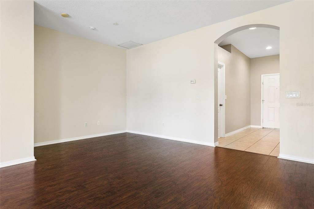 An empty room with dark wood-look flooring and an arched entryway leading to a foyer — 3033 GEM LUSTER COURT, VALRICO, FL