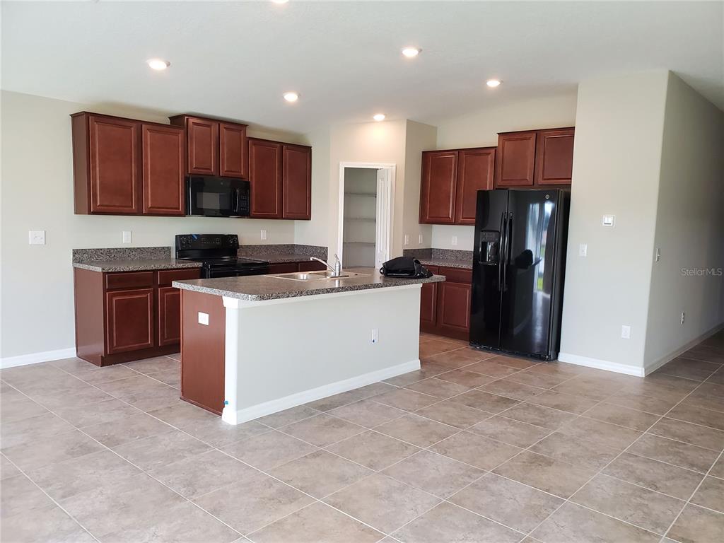 A kitchen features dark wood cabinets, granite countertops, a center island, and black appliances — 10117 BERRYESSA AVENUE, RIVERVIEW, FL
