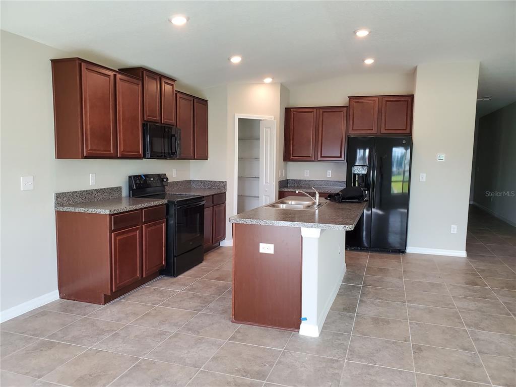 A kitchen with dark wood cabinets, black appliances, a center island, and tile flooring — 10117 BERRYESSA AVENUE, RIVERVIEW, FL