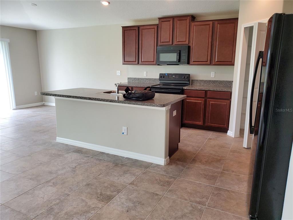 A kitchen features dark wood cabinets, granite countertops, a center island, and tile flooring — 10117 BERRYESSA AVENUE, RIVERVIEW, FL