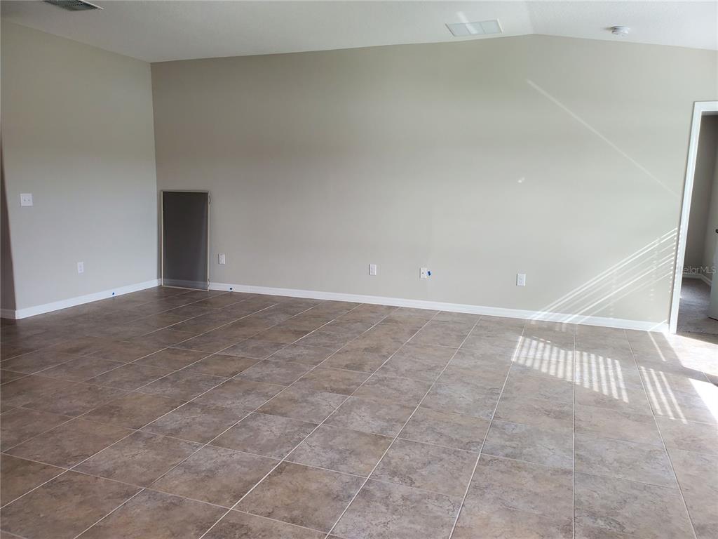 An empty room features beige walls, tiled flooring, and a small access panel — 10117 BERRYESSA AVENUE, RIVERVIEW, FL
