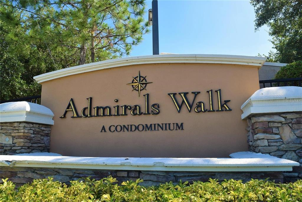 A tan monument sign for Admirals Walk A Condominium stands outdoors with stone accents — 5581 ROSEHILL ROAD UNIT # 203, SARASOTA, FL