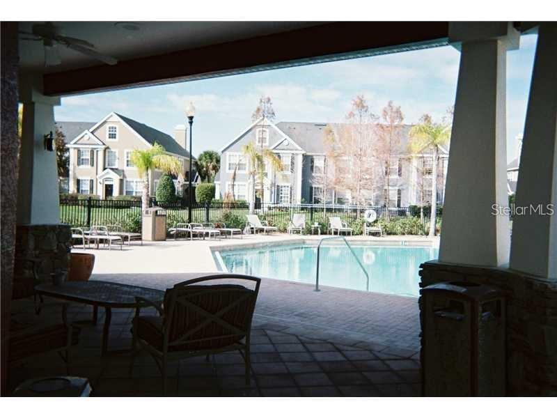 A covered patio overlooks a swimming pool surrounded by a fence and residential buildings — 5581 ROSEHILL ROAD UNIT # 203, SARASOTA, FL