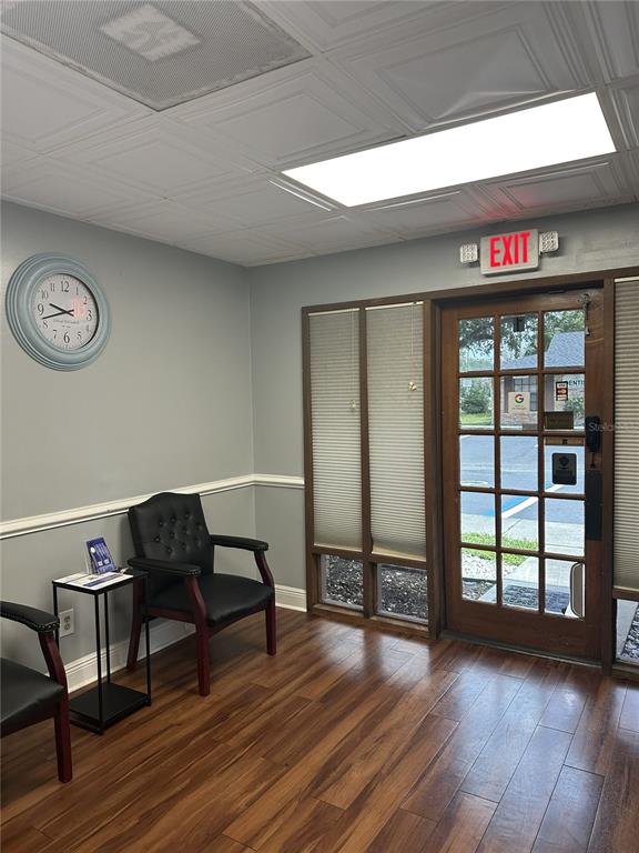 A waiting room with wood-look flooring, two black chairs, a wall clock, and a glass door — 318 N JOHN YOUNG PARKWAY UNIT 101, KISSIMMEE, FL
