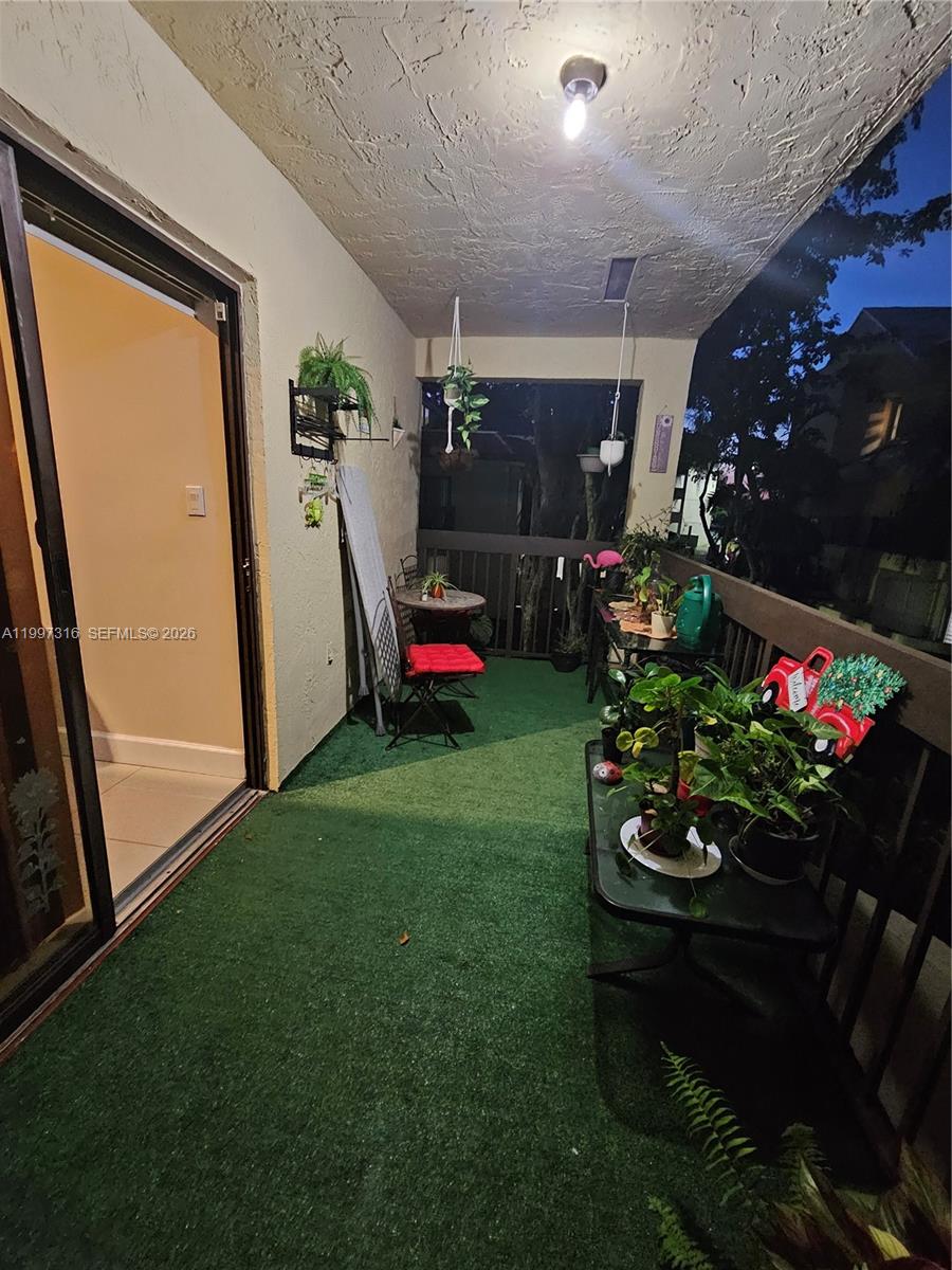 A covered balcony features artificial turf flooring, potted plants, and outdoor furniture at dusk — 13063 SW 88th Ter S # B, Miami FL 33186, MIAMI, FL