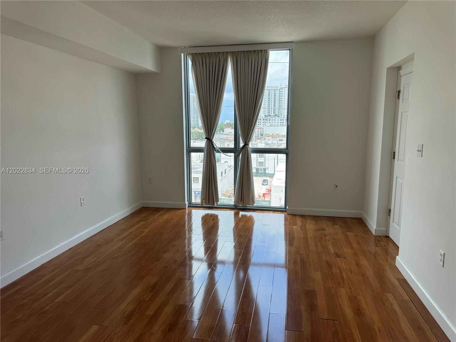 An empty room features hardwood floors, white walls, and a large window with curtains — 140 S Dixie Hwy # 521, Hollywood FL 33020, HOLLYWOOD, FL