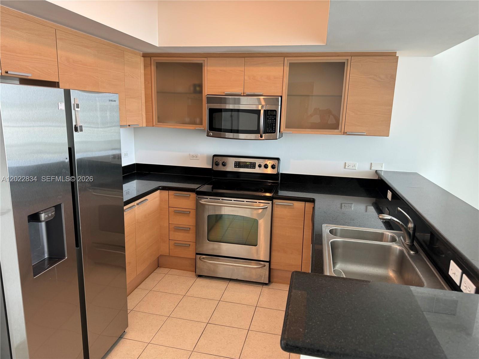 A kitchen features light wood cabinets, black countertops, stainless steel appliances, and tiled flooring — 140 S Dixie Hwy # 521, Hollywood FL 33020, HOLLYWOOD, FL