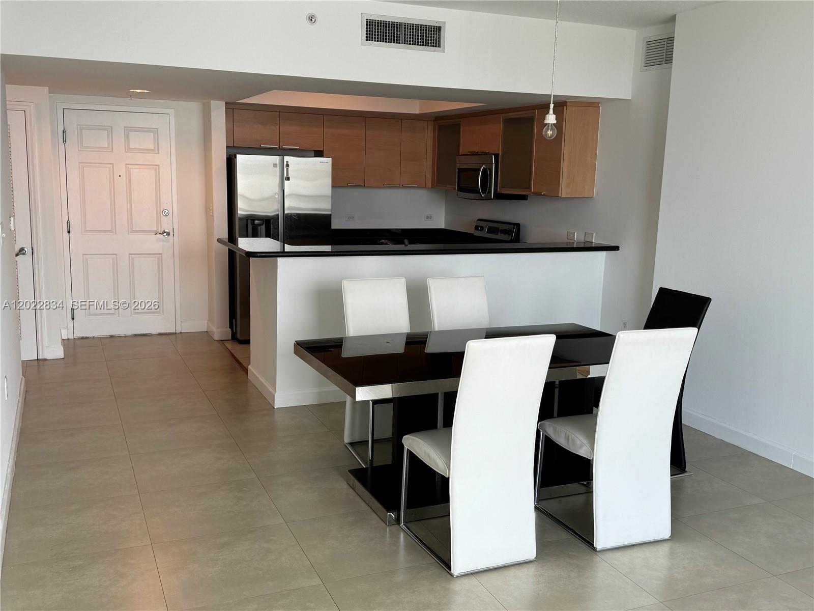 A dining area with a black table and white chairs sits before a kitchen — 140 S Dixie Hwy # 521, Hollywood FL 33020, HOLLYWOOD, FL