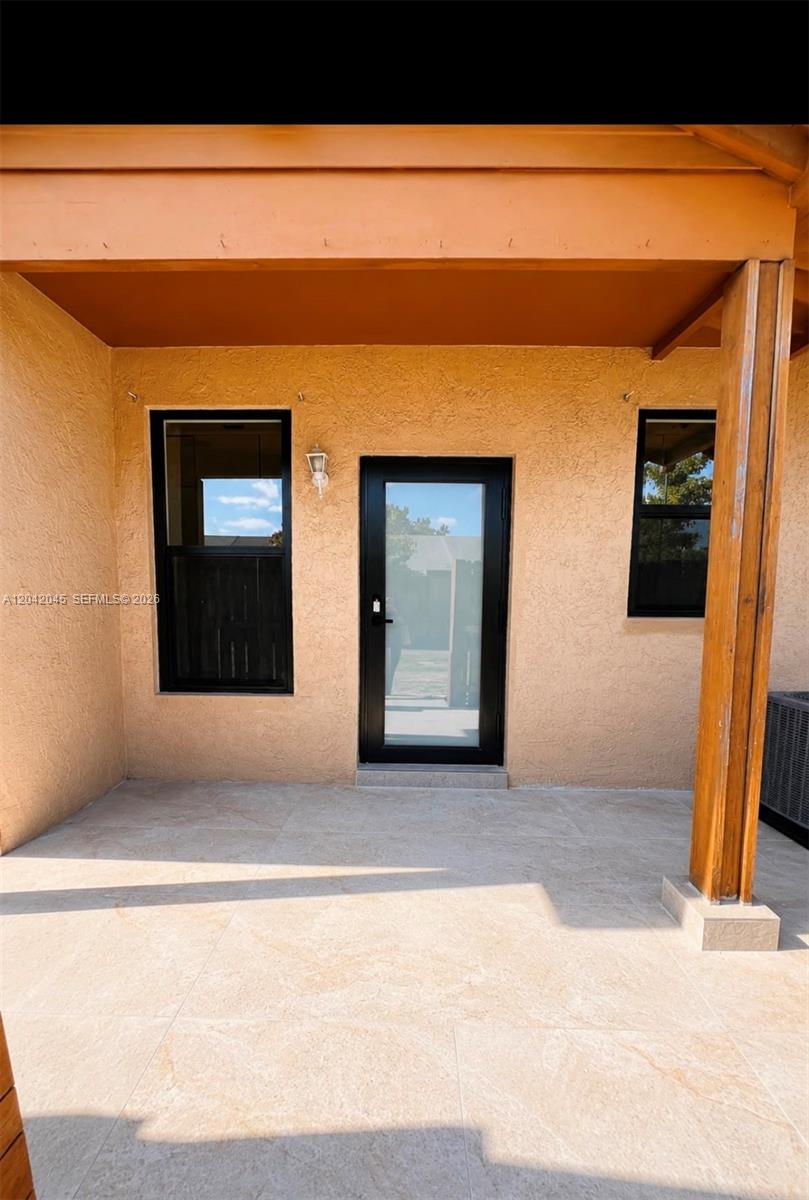 A covered patio features light-colored tile flooring, stucco walls, and a black-framed glass door — 6780 NW 186th Ter, Hialeah FL 33015, HIALEAH, FL