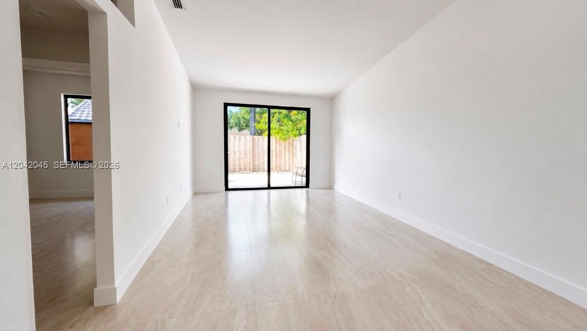 A bright, empty room features light-colored tile flooring, white walls, and sliding glass patio doors — 6780 NW 186th Ter, Hialeah FL 33015, HIALEAH, FL
