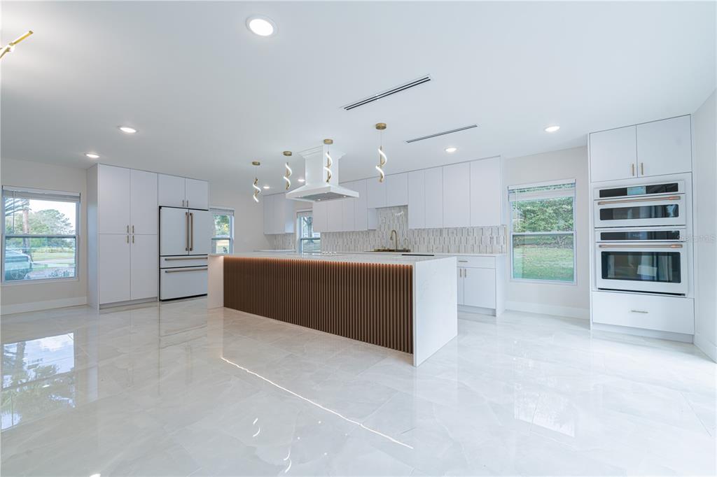 A modern white kitchen features a slatted wood island, marble floors, and stainless steel appliances — 2721 INGEBORG COURT, WINDERMERE, FL