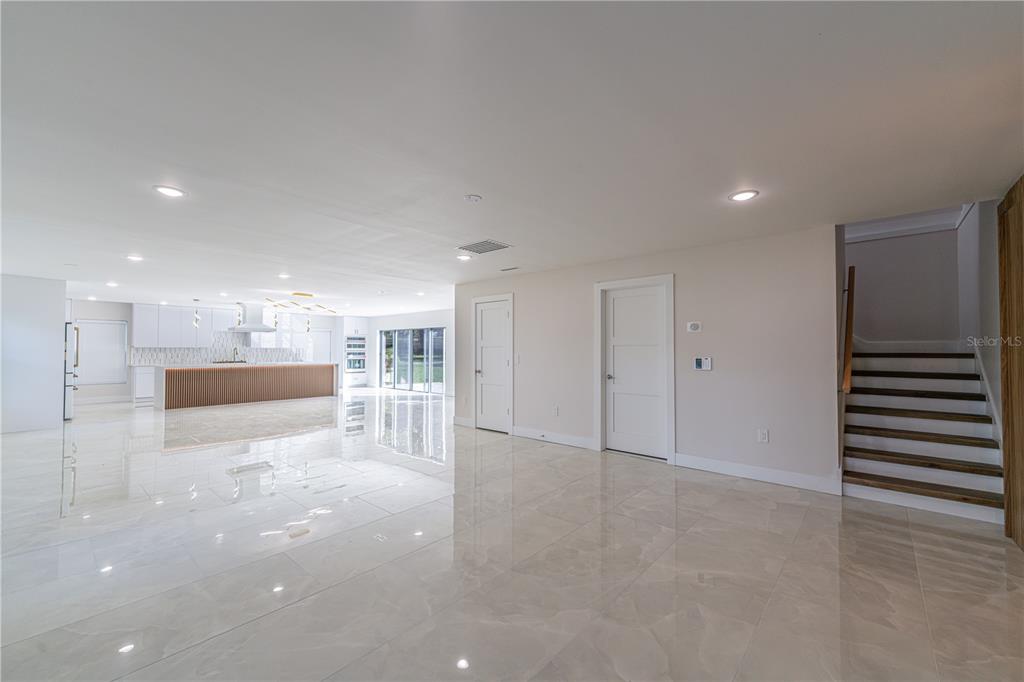 A spacious, open-concept room features white tile flooring, a modern kitchen, and a wooden staircase — 2721 INGEBORG COURT, WINDERMERE, FL