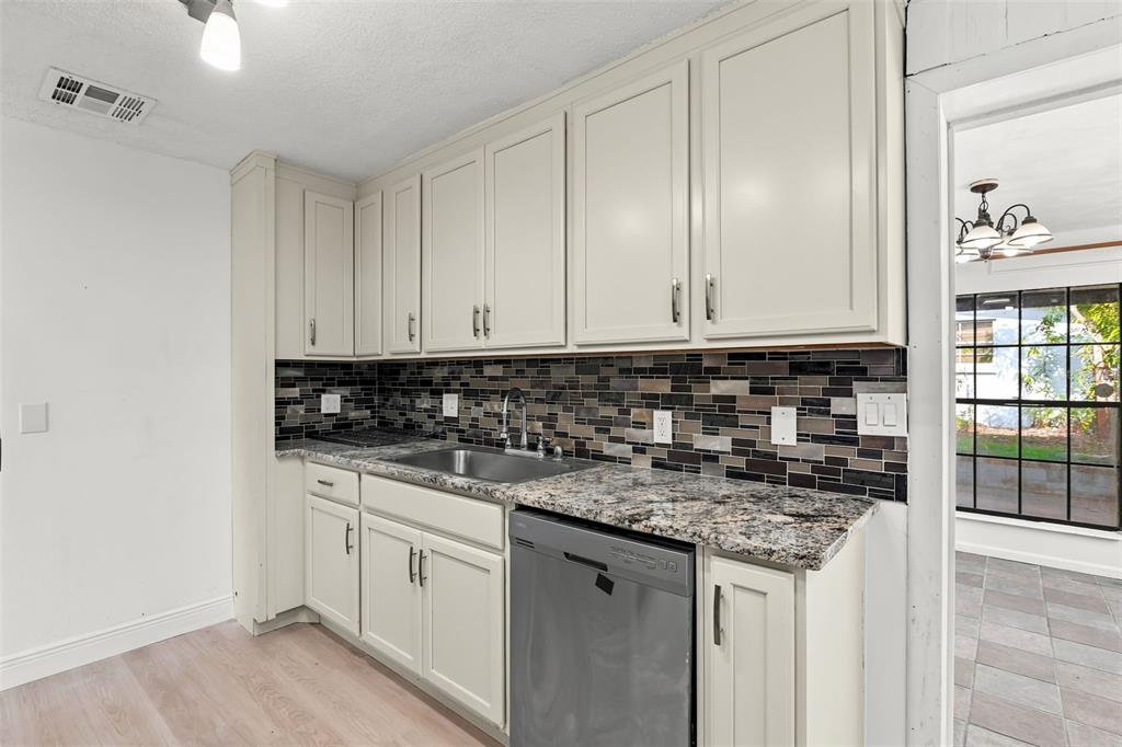 A kitchen features light-colored cabinets, granite countertops, a tiled backsplash, and a stainless steel dishwasher — 1432 RICHMOND AVENUE, DAYTONA BEACH, FL
