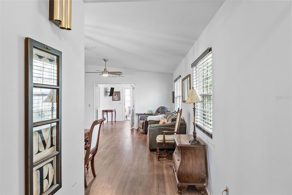 A hallway with wood-look flooring leads into a living room with a ceiling fan — 37420 TEABERRY LOOP, ZEPHYRHILLS, FL