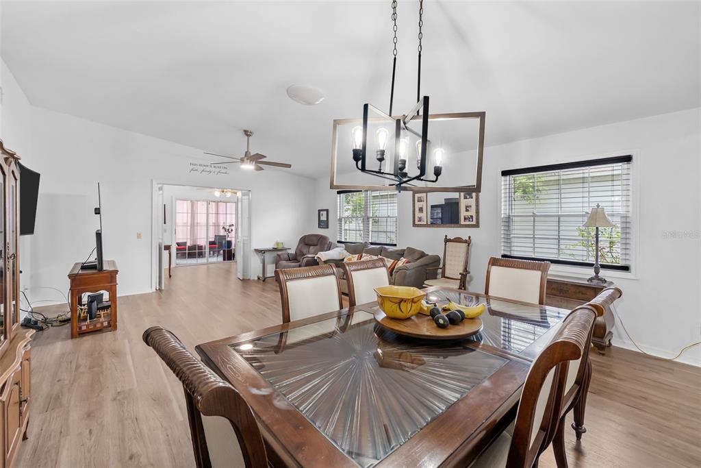 A dining area with a glass-topped table and chandelier opens into a living room space — 37420 TEABERRY LOOP, ZEPHYRHILLS, FL