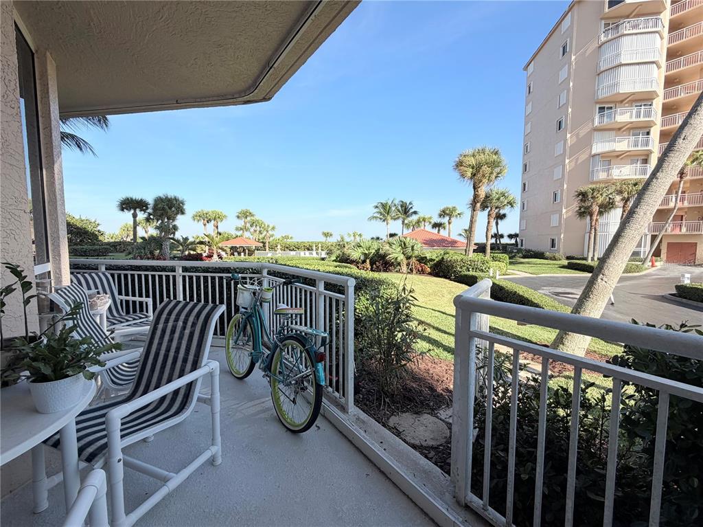 A balcony with striped chairs, a bicycle, and a view of palm trees and buildings — 3880 N HIGHWAY A1A UNIT 104, HUTCHINSON ISLAND, FL