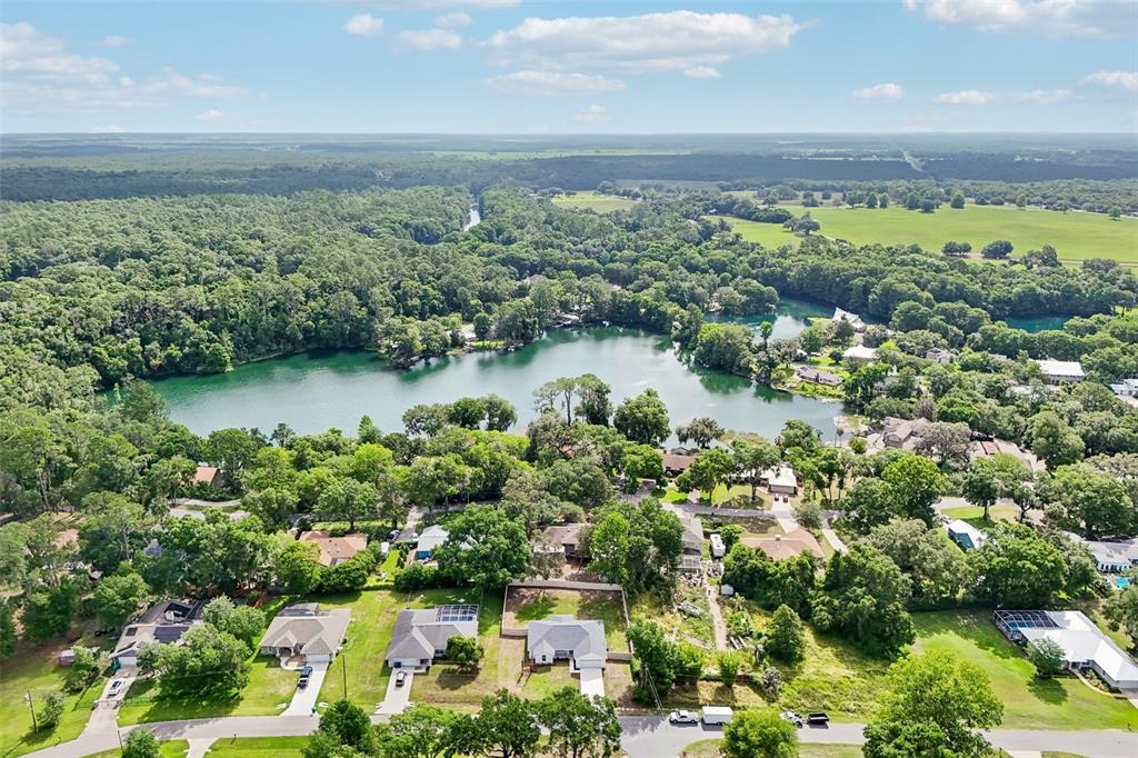 An aerial view shows houses situated near a lake surrounded by dense green trees — 11591 MOCKINGBIRD DRIVE, DUNNELLON, FL