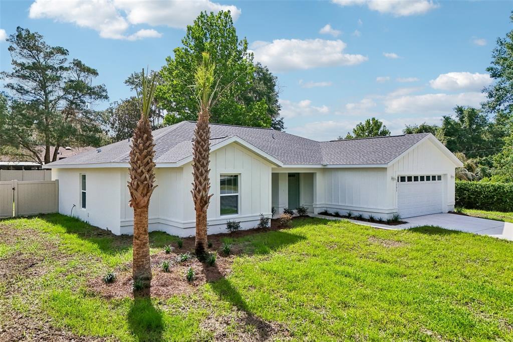 A white single-story house with vertical siding, a gray shingled roof, and two palm trees — 11591 MOCKINGBIRD DRIVE, DUNNELLON, FL