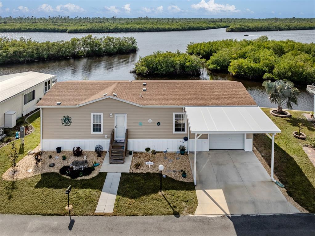 An aerial view of a tan manufactured home with a carport and waterfront backyard — 106 ISLAND POINT ROAD, NORTH PORT, FL
