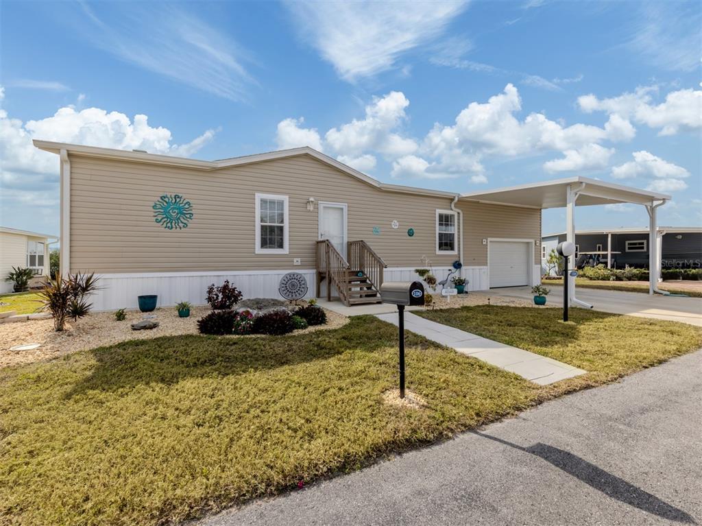A tan manufactured home features a front porch, a carport, and a small landscaped yard — 106 ISLAND POINT ROAD, NORTH PORT, FL