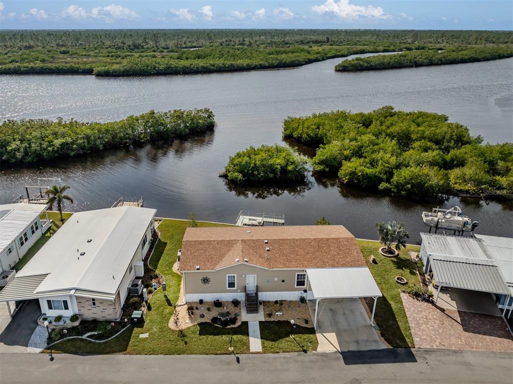 An aerial view shows three waterfront houses with carports along a river lined with mangroves — 106 ISLAND POINT ROAD, NORTH PORT, FL