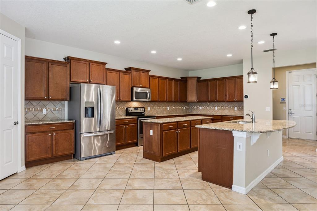 A kitchen features wood cabinets, granite countertops, stainless steel appliances, and a central island — 13328 OVERSTREET ROAD, WINDERMERE, FL