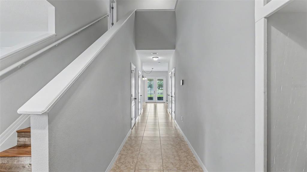 A hallway with light-colored tile flooring leads to glass doors under a staircase — 2746 WALDEN WOODS DRIVE, PLANT CITY, FL