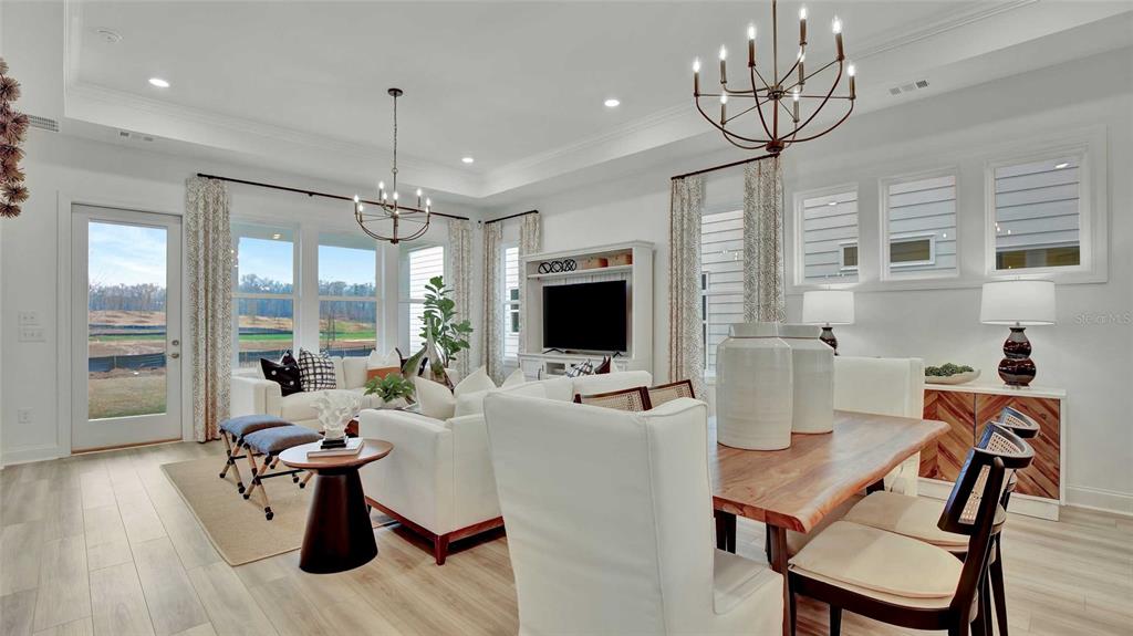 A bright, open-concept living and dining area features white furniture, wood flooring, and chandeliers — 1533 TREGAN AVENUE, DELAND, FL